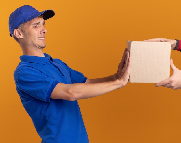 Someone gives cardbox to unpleased young blonde delivery boy pushing cardbox back on orange