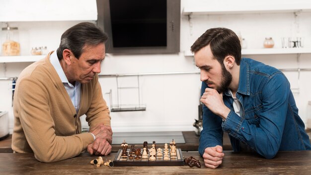 Сын и папа играют в шахматы на кухне
