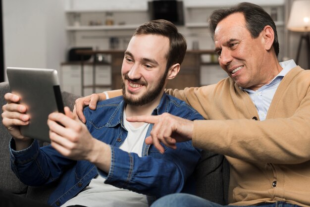 Son and father smiling and looking at tablet in living room
