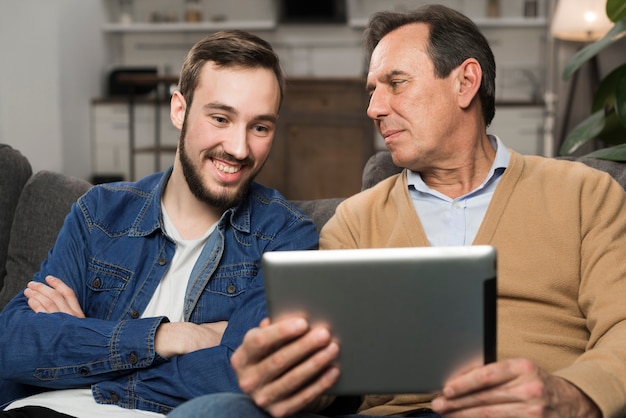 Son and father smiling at tablet in living room