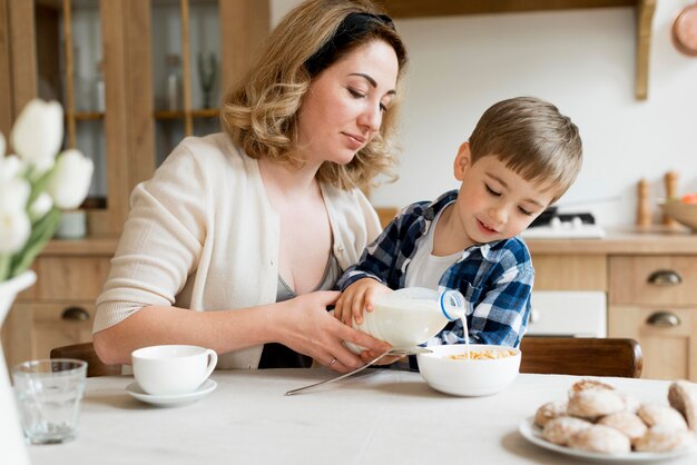 Son helping her mother pouring milk in bowl