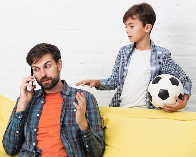 Foto gratuita figlio che tiene una palla e padre che parla sul telefono