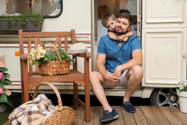 Son hugging his father while sitting on caravan