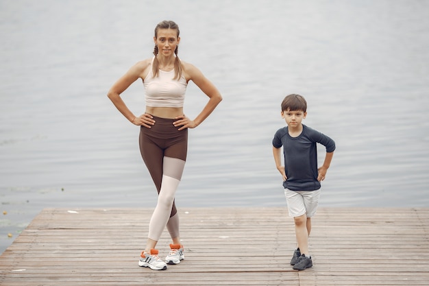 Son and mother are doing exercises in the summer park. Family by the water.