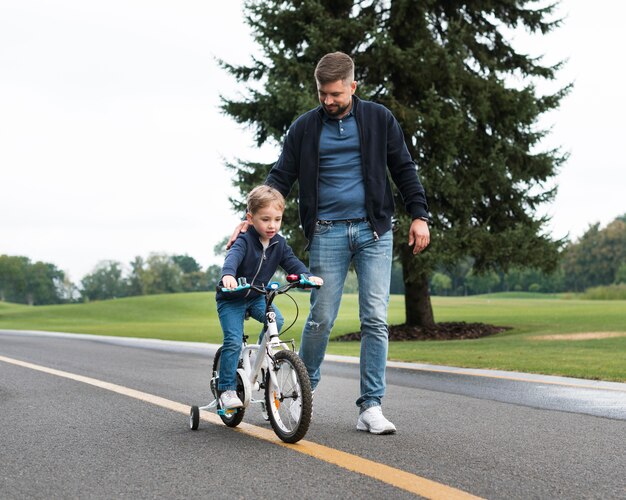 Son riding a bike in the park alongside his father