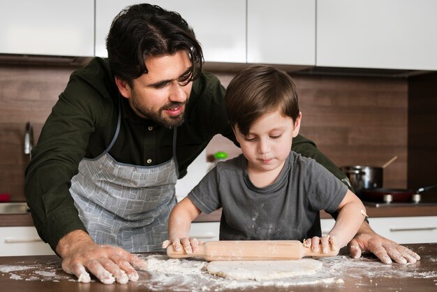 Son rolling dough under father watch