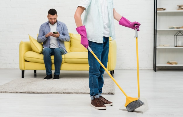 Son using broom while father checks phone