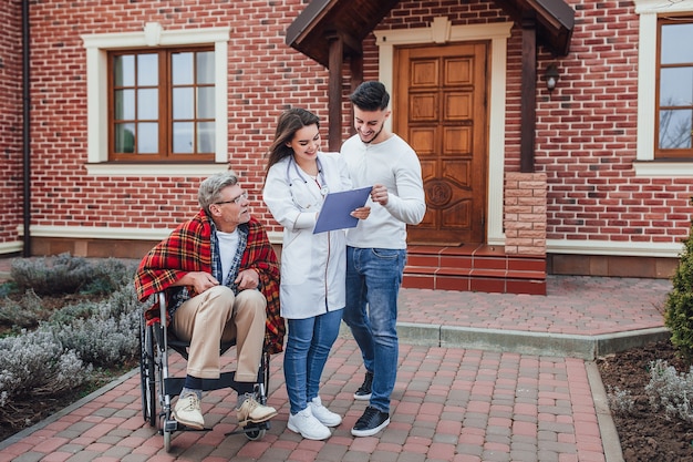 Son with nurse speaking about old man in whelchair and looking on his results