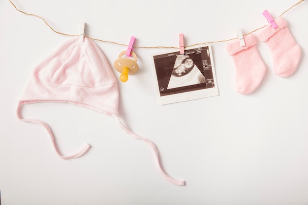 Sonography; headwear; pacifier and sock hanging on clothesline over white backdrop