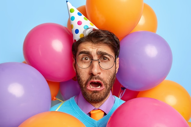 Sorrowful discontent guy surrounded by party balloons posing