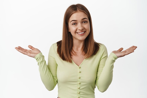 Sorry cant help you. Unbothered smiling girl shrugging shoulders unaware, being clueless, dont know and not care, standing against white background, nothing to say