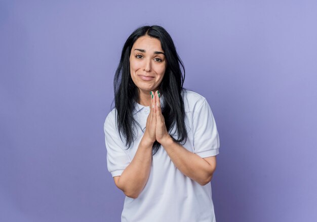 Sorry young brunette caucasian girl holds hands together isolated on purple wall