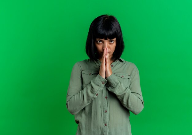 Free photo sorry young brunette caucasian woman holds hands together looking at camera isolated on green background with copy space