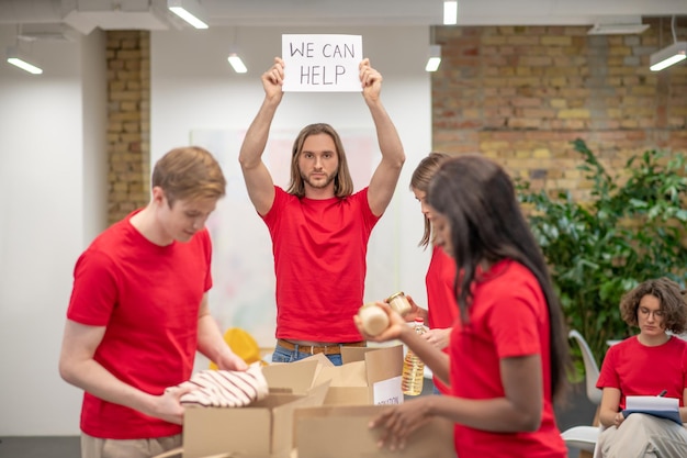 Сортировочный центр. Молодые волонтеры в красных футболках раздают пожертвования в сортировочном центре