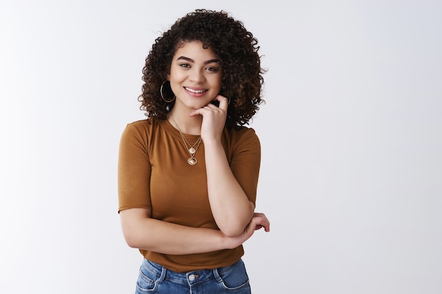 Sounds interesting. Curious good-looking happy smiling curly-haired girl listening have pleasant funny conversation touch cheek grinning nod agree speaking coworker lunch-break, white background