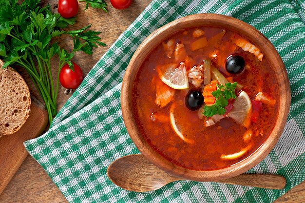 Soup solyanka Russian with meat, olives and gherkins in wooden bowl