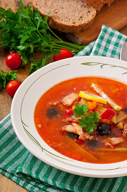 Soup solyanka Russian with meat, olives and gherkins in wooden bowl