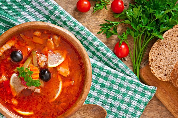 Soup solyanka Russian with meat, olives and gherkins in wooden bowl