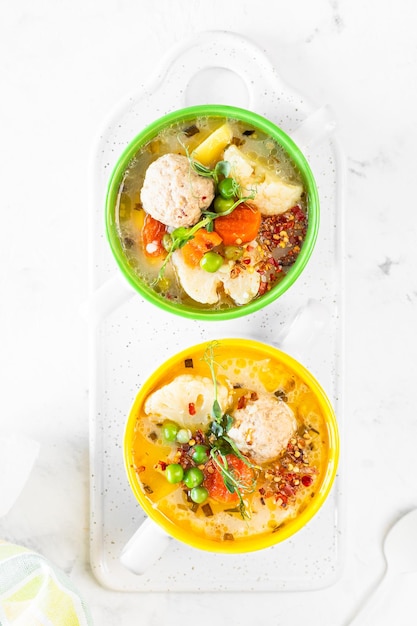 Soup with chicken meatballs and spring vegetables on a white background Vertical