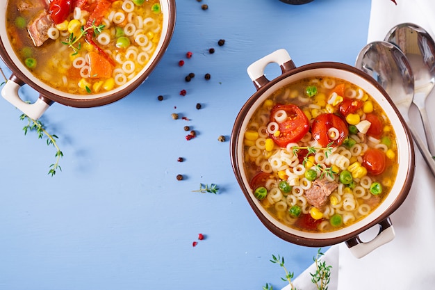 Soup with small pasta, vegetables and pieces of meat in  bowl on  blue table. Italian food. Top view. Flat lay