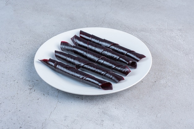 Free photo sour cherry plum snack rolls on a white platter on marble background.