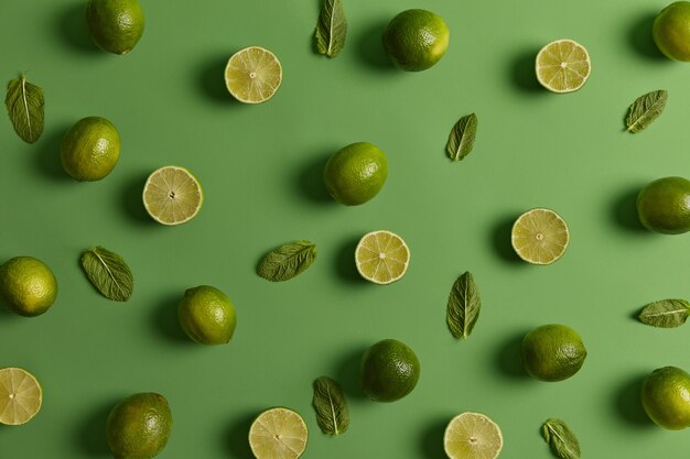 Sour green bright limes loaded with nutrients and fresh mint on green background. Citrus fruit can boost your immunity system, promote healthy skin. Floral aroma of zest, ingredients valued for juice