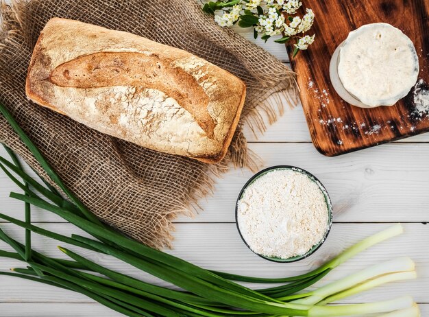 白い木製のテーブルでパン、小麦粉、焼きたてのパンを作るためのサワードウ