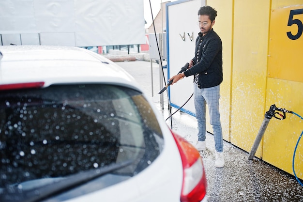 Uomo del sud asiatico o maschio indiano che lava il suo trasporto bianco sull'autolavaggio