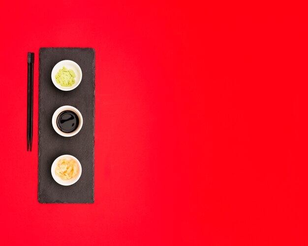 Soy sauce; wasabi and ginger on a stone plate over red backdrop with space for text