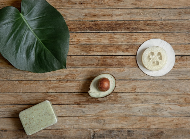 Spa composition with natural soap, avocado and loofah on a wooden surface top view.