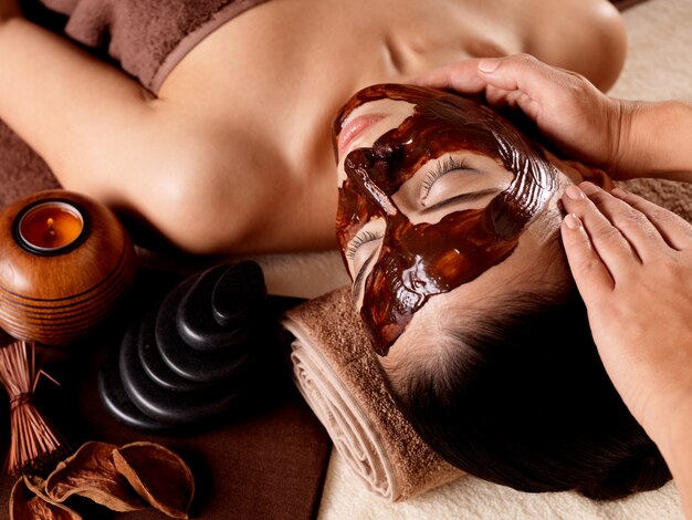 Spa massage for young woman with facial mask on face - indoors