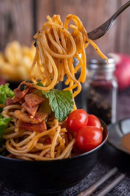 Спагетти в черной чашке с помидорами и листьями салата.