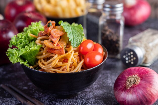 Spaghetti in a black cup with tomatoes and lettuce.