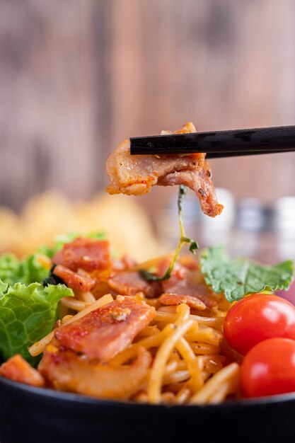 Spaghetti in a black cup with tomatoes and lettuce.