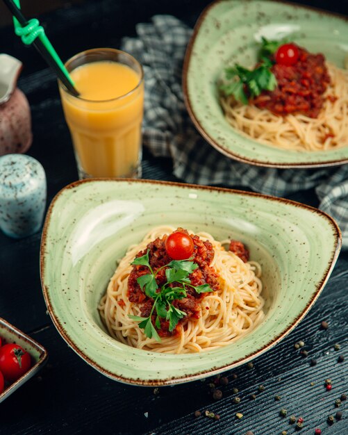 Спагетти в соусе Болоньез, зелень и помидоры в зеленой тарелке и апельсиновый сок вокруг.