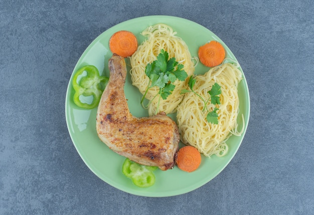 Спагетти и жареная нога на зеленой тарелке.