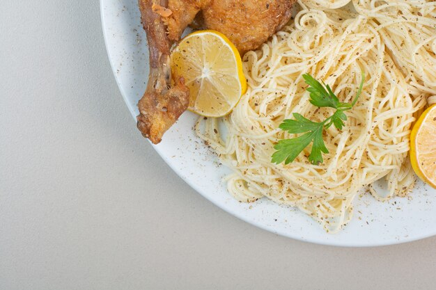 Spaghetti, lemon and chicken leg on white plate