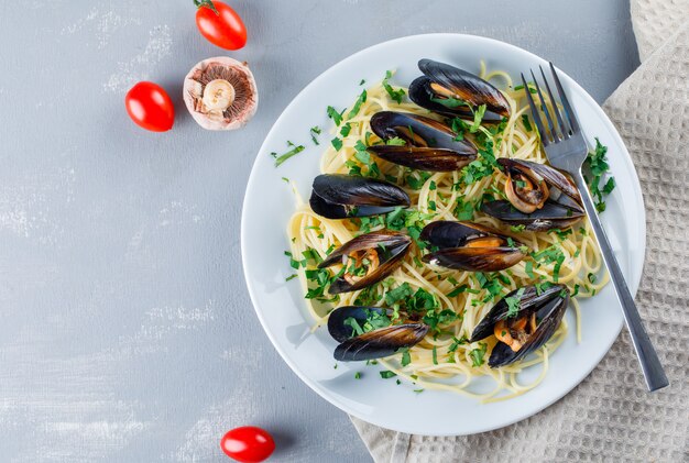 Spaghetti and mussel with tomatoes, mushroom, fork in a plate on kitchen towel