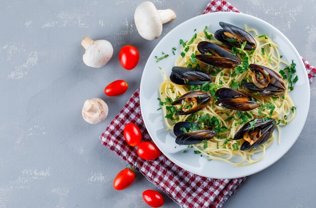 Spaghetti and mussel with tomatoes, mushrooms in a plate on plaster and kitchen towel