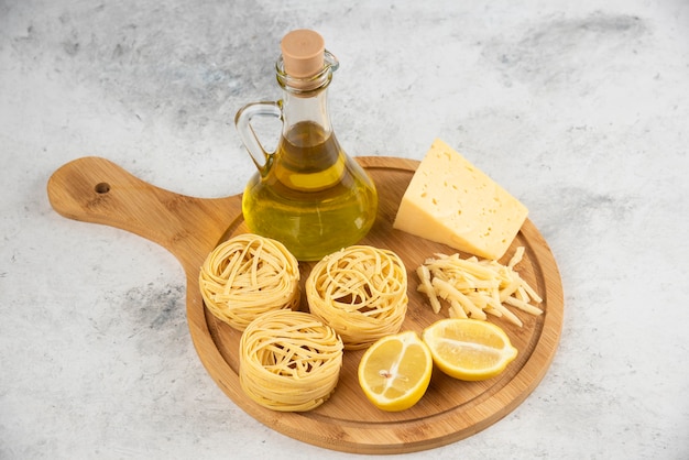 Nidi di spaghetti, olio, formaggio lemonnd su tavola di legno.