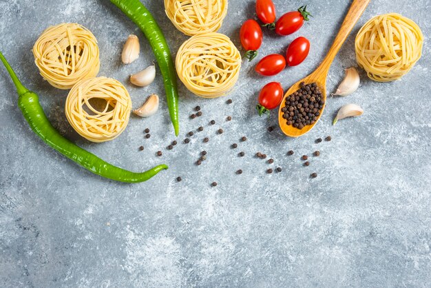 Spaghetti nests, peppers and tomatoes on marble background.
