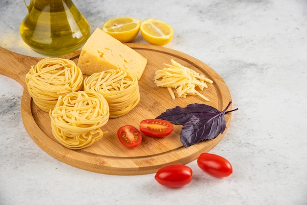 Гнезда спагетти, овощи и сыр на деревянной доске.