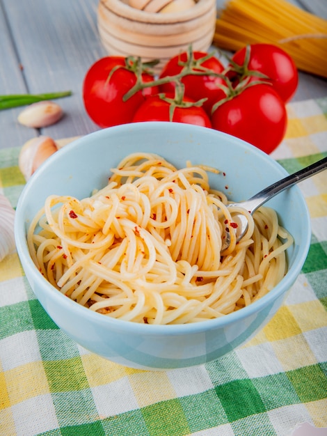 Spaghetti pasta with chili flakes in a white bowl with fork and fresh tomatoes on a tablecloth