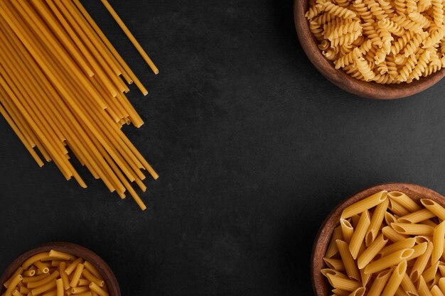 Спагетти и макаронные изделия на черном фоне, вид сверху.