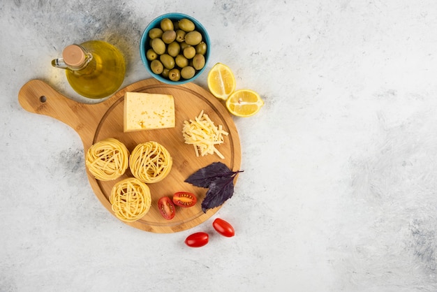 Spaghetti, vegetables and cheese on wooden board with olives.