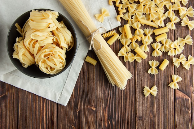 Spaghetti with assorted raw pasta on wooden and kitchen towel background, flat lay.