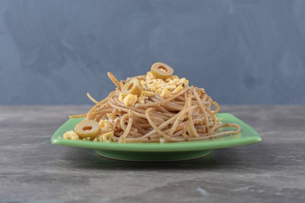 Spaghetti with fried eggs on green plate.