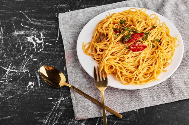 Спагетти с зеленью и овощами в белой тарелке, вид сверху
