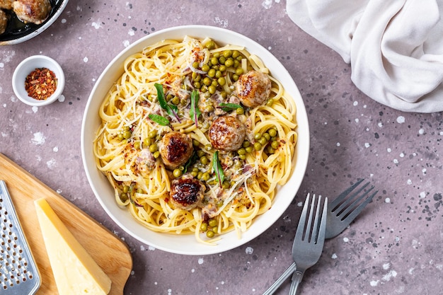 Спагетти с мясными шариками и сливочным соусом подают на тарелке с травами и пармезаном