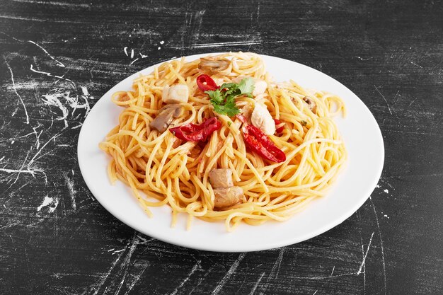 Spaghetti with mixed ingredients in a white plate on black background, top view. 